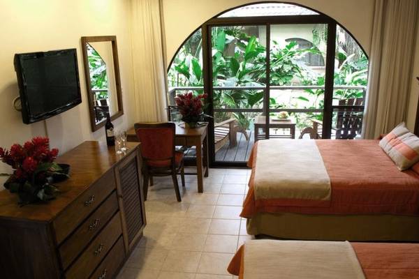 Schlafzimmer im Punta Leona Hotel mit zwei Betten, Fernseher, Spiegel und Möbeln.