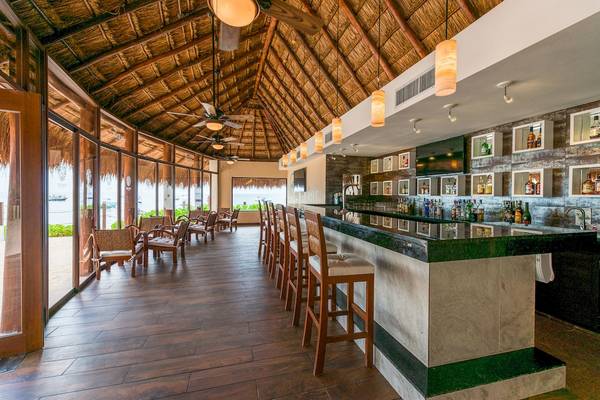 Innenansicht der Bar im Reef Coco Beach Hotel mit Barhockern, Theke und Fenstern.