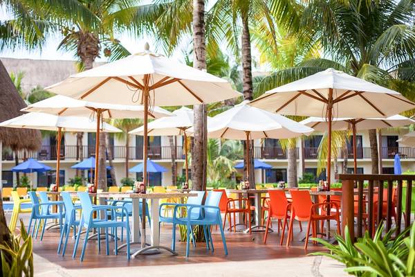 Terrasse im Reef Coco Beach Hotel mit mehreren weißen Sonnenschirmen und bunten Stühlen.