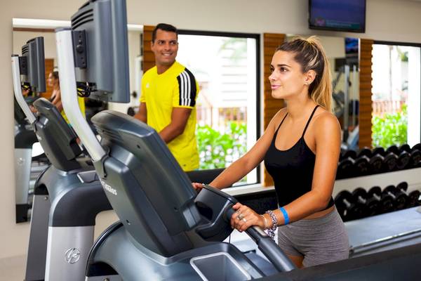 Fitnessstudio im Reef Coco Beach Hotel mit einer Frau auf dem Laufband und einem Mann im Hintergrund.