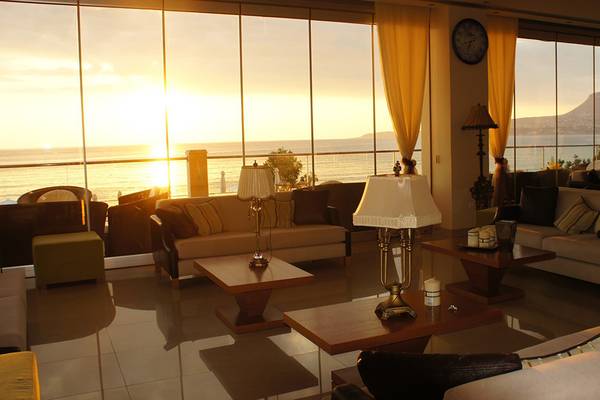 Wohnbereich im Kiani Beach Resort mit großen Fenstern und Meerblick bei Sonnenuntergang.