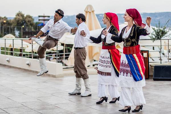 Vier Personen in traditioneller griechischer Kleidung tanzen auf der Terrasse des Kiani Beach Resorts.