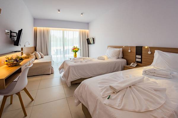 Zwei Betten in einem Hotelzimmer des Kiani Beach Resort, beide mit weißen Laken und Kissen, ein Bett hat einen Tisch und eine Vase mit Blumen.