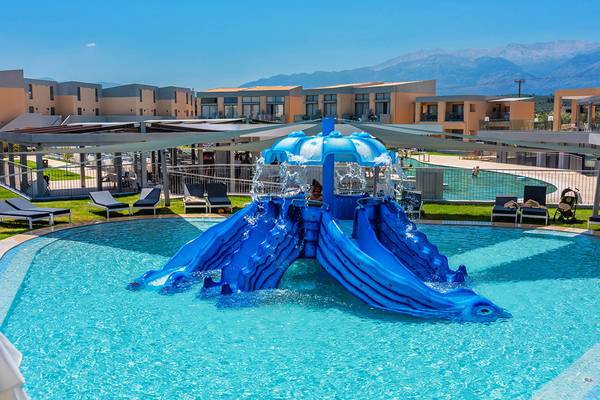 Blaue Wasserrutsche im Pool des Kiani Beach Resort mit Gebäuden und Bergen im Hintergrund.