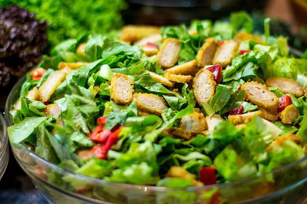Ein Salat mit grünem Blattwerk, gewürfeltem Huhn und roten Paprikastücken in einer Glasschale.