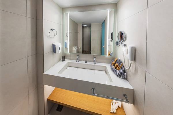 Badezimmer im Kiani Beach Resort mit Waschbecken, Spiegel und Toilettenartikeln.