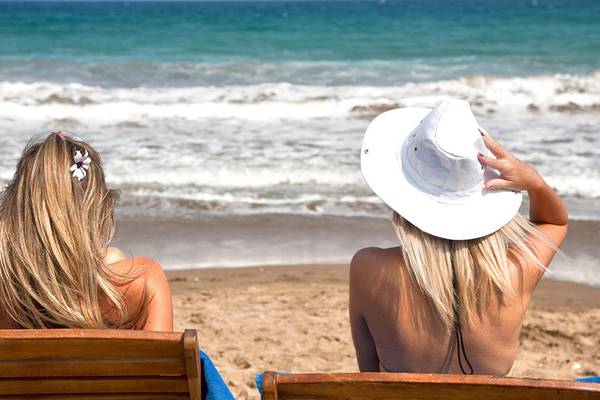Zwei Frauen im Bikini liegen auf Strandliegen und genießen die Aussicht auf das Meer.