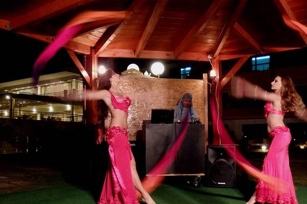 Zwei Frauen in pinken Kostümen führen eine Bauchtanz-Aufführung unter einem Pavillon im Kiani Beach Resort durch, während ein DJ im Hintergrund spielt.