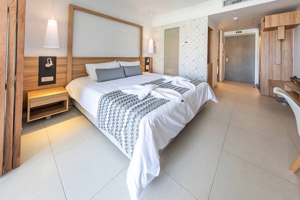 Schlafzimmer im Kiani Beach Resort mit modernem Design, Doppelbett, Nachttischen und weißen Fliesen.