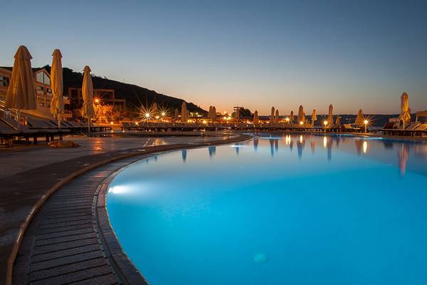 Kiani Beach Resort Swimmingpool bei Sonnenuntergang mit Lounge-Stühlen und Sonnenschirmen
