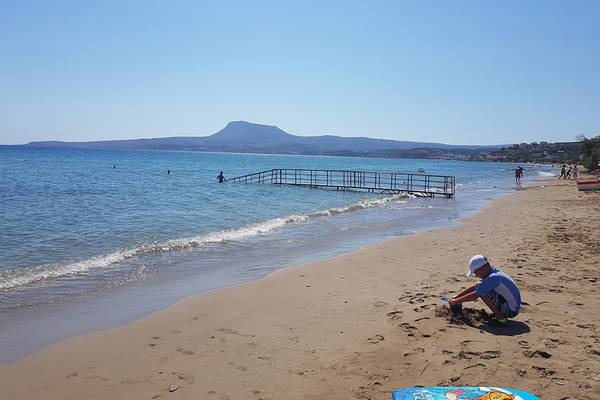 Strand des Kiani Beach Resort mit spielendem Kind und Panoramablick auf das Meer und Berge.