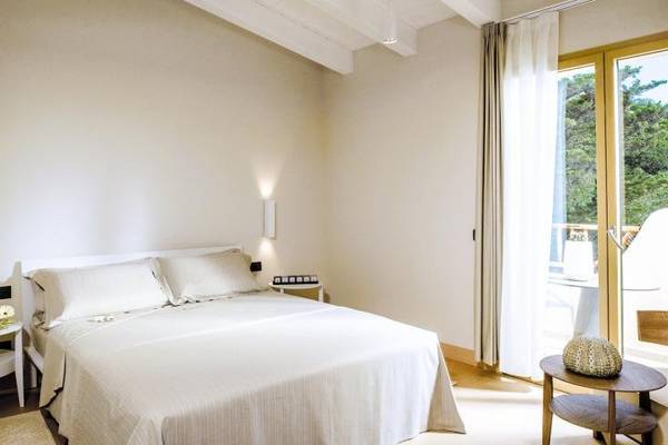 Schlafzimmer im Hotel Cala Cuncheddi mit einem Bett, Kissen, Tisch und Aussicht auf Bäume.