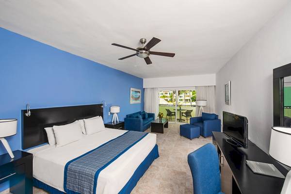 Innenansicht eines Zimmers im Ocean Blue & Sand by H10 Hotel mit einem großen Bett, blauen Möbeln und einer Terrasse