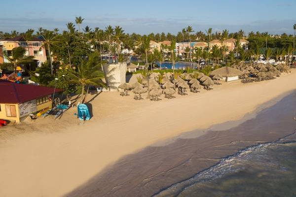 Luftaufnahme des Ocean Blue & Sand by H10 Hotel am Strand mit Gebäuden, Bäumen und Sonnenschirmen.