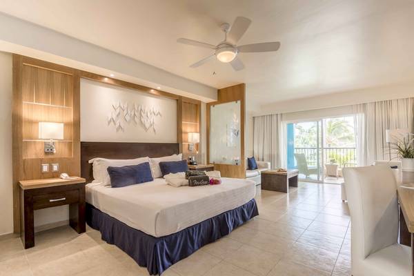Schlafzimmer im Ocean Blue & Sand by H10 Hotel mit Bett, Nachttischen, Lampe, Deckenventilator und Balkon.
