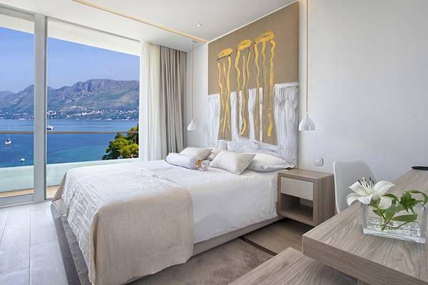 Ein elegantes Schlafzimmer im Cavtat Hotel mit Meerblick, einem großen Bett, weißen Laken, Kissen und einer Wanddekoration.