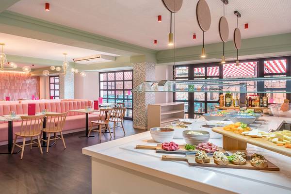 Innenbereich des Aparthotel Allegro Isora mit bunten Wänden, pinken Bänken und verschiedenen Tischen und Stühlen.