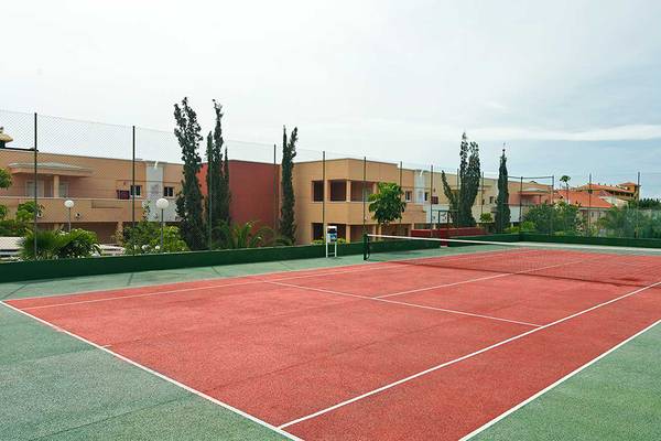 Tennisplatz im Aparthotel Allegro Isora mit roten Belägen und Gebäuden im Hintergrund.