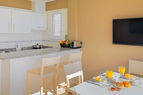 Küche und Essbereich im Aparthotel Allegro Isora mit Frühstückstisch, Fernseher und Obstkorb.