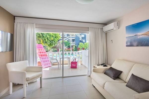 Wohnzimmer im Aparthotel Allegro Isora mit einer weißen Couch, einem weißen Sessel, einer Terrasse und einem Swimmingpool.