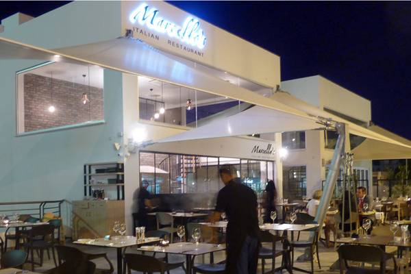 Foto des Marcella's Italian Restaurant Außenbereichs bei Nacht mit Gästen an den Tischen und einem Mitarbeiter, der bedient.