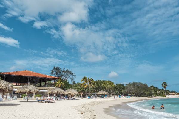 Strand des Zoetry Curacao Resort & Spa mit Sonnenschirmen und Liegen unter blauem Himmel