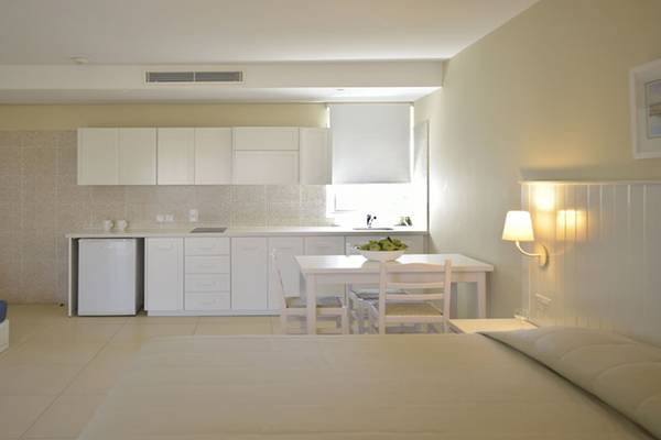 Suite mit Schlafzimmer und Küche im Sunrise Gardens Hotel, mit hellen Möbeln und einer kleinen Essecke.
