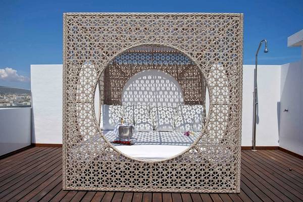 Lounge-Bereich auf der Dachterrasse des Torre del Mar Hotels mit einem gewebten Pavillon, Kissen, einer Flasche und einem Silbereimer.