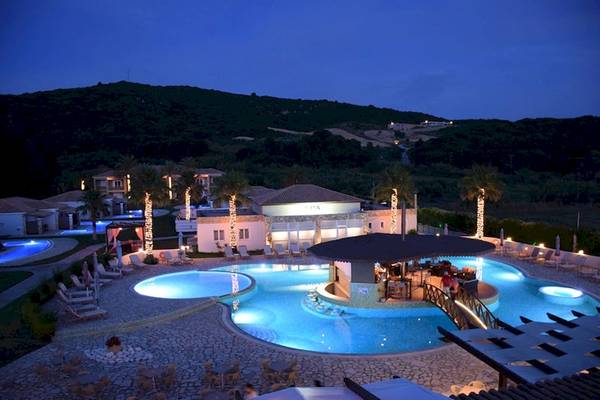 Abendansicht des Olympia Golden Beach Resorts mit Swimmingpool, Bar und Loungebereichen.