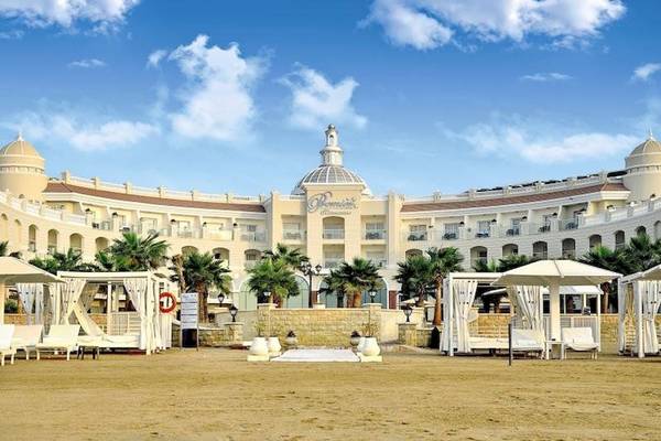 Außenansicht des KaiSol Romance Resort Sahl Hasheesh mit weißen Liegen und Sonnenschirmen am Strand.