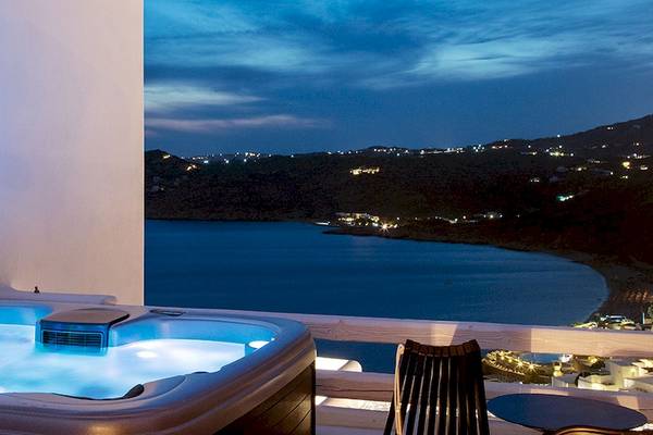 Jacuzzi auf dem Balkon des Myconian Avaton Resorts bei Nacht mit Blick auf die Stadt und das Meer.