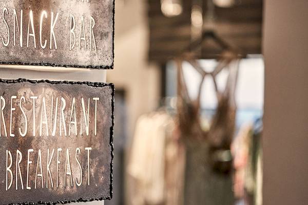 Weiß beleuchtete Schilder an einer Wand im Myconian Avaton Resort, die Snack Bar und Restaurant Breakfast anzeigen.