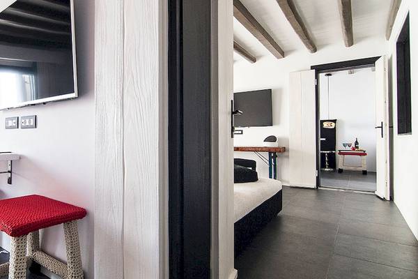 Hotelzimmer im Myconian Avaton Resort mit Fernseher an der Wand, rotem Stuhl und Tisch.