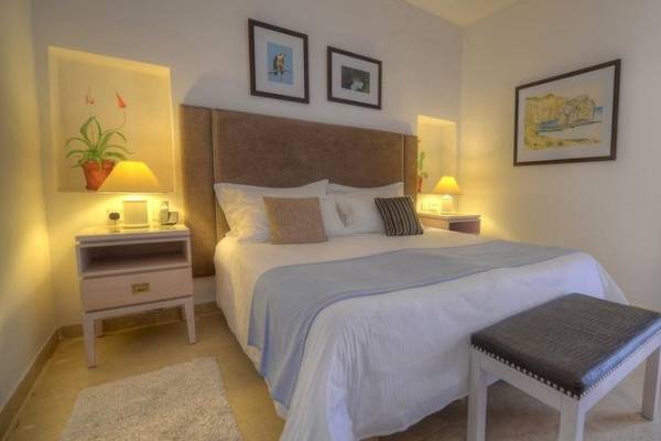 Schlafzimmer im Hotel Ta' Cenc & Spa mit zwei Nachttischen, Kissen, Lampe und Gemälden an der Wand.
