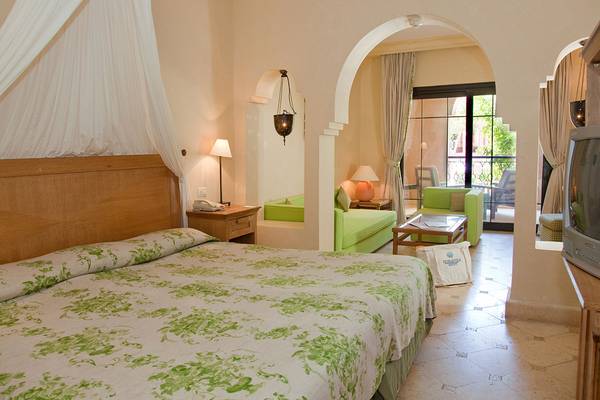 Makadi Palace Zimmer mit grünem Bett und Wohnzimmerbereich.