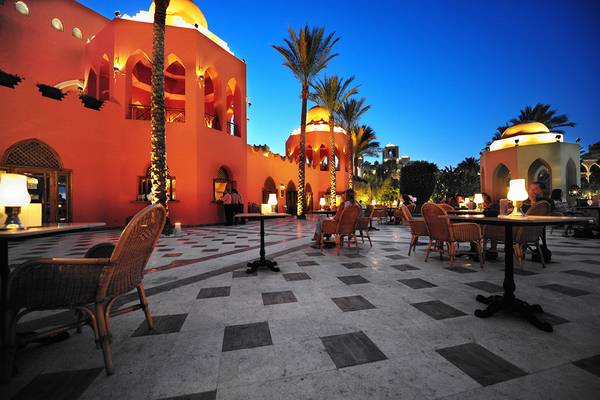 Außenbereich des Makadi Palace Hotels bei Nacht mit beleuchteten Gebäuden, Tischen und Palmen.