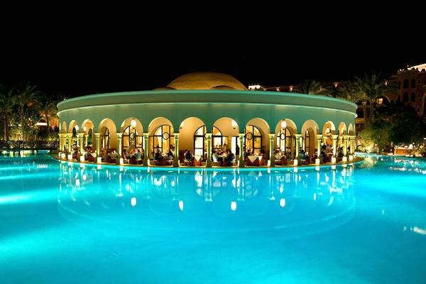 Makadi Palace Hotel Pool bei Nacht mit beleuchteten Arkaden und Gästen.