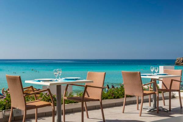 Terrasse des Nissi Beach Resorts mit Tischen und Blick auf das Meer.
