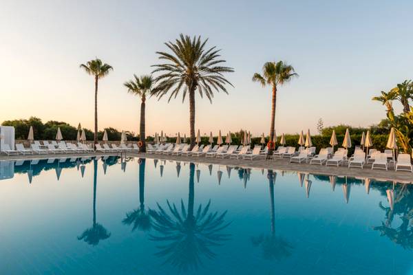 Ein Außenpool am Nissi Beach Resort mit vielen Sonnenliegen und Palmen im Hintergrund