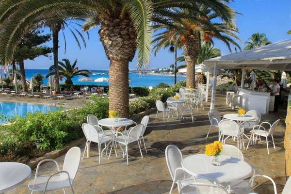 Außenterrasse des Nissi Beach Resorts mit Tischen, Stühlen und Blick auf den Pool und das Meer.