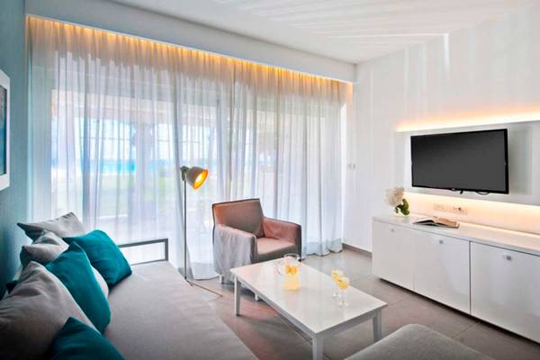 Wohnzimmer im Nissi Beach Resort mit Fernseher, Couch, Tisch, Stuhl und Lampe.