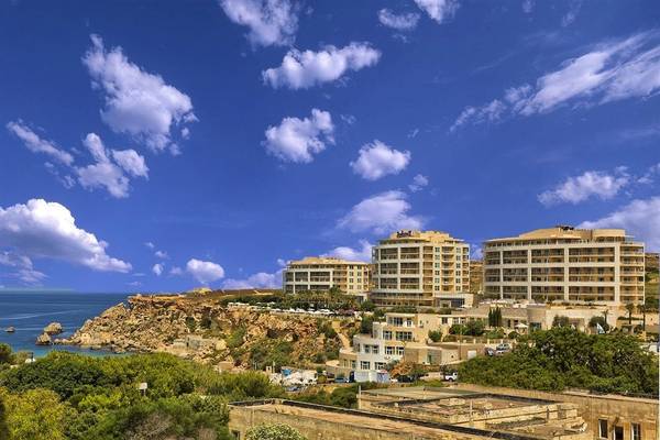 Aussicht auf das Radisson Blu Resort & Spa, Malta Golden Sands, mit Gebäuden, Meer und blauem Himmel.