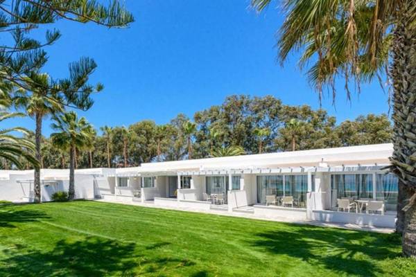 Außenbereich des Nissi Beach Resorts mit weißen Gebäuden, Palmen und Rasen.