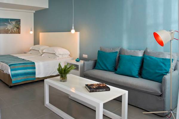 Innenansicht eines Hotelzimmers im Nissi Beach Resort mit Doppelbett, Sofa, Tisch und Lampen.