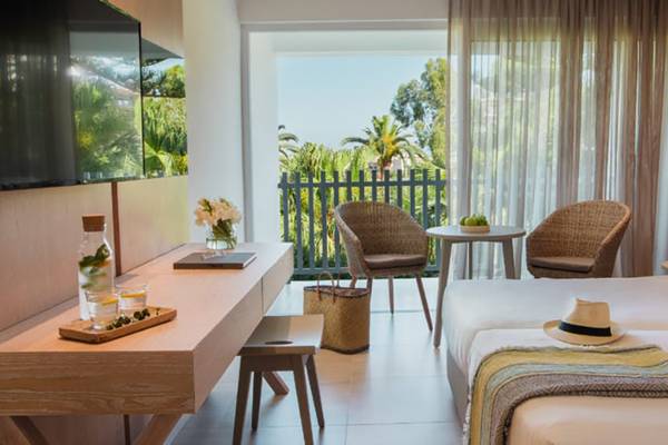 Innenansicht eines Hotelzimmers im Nissi Beach Resort mit Blick auf einen Balkon und Palmen.