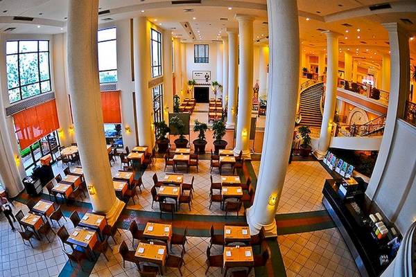 Luftaufnahme des Speisesaals im Charmillion Club Resort mit vielen Tischen und Stühlen, hohen Säulen und einer Treppe.