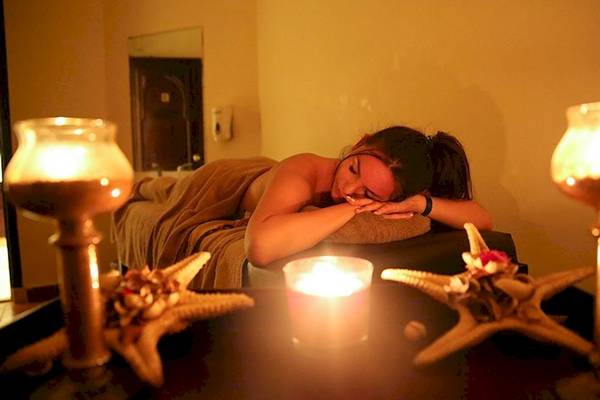 Eine Frau liegt entspannt in einem Hotel-Spa-Bereich mit Kerzen und Sternenfischen.