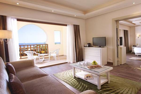 Innenansicht der Suite im Charmillion Club Resort mit Wohnzimmer, Fernseher, Tisch und Balkon