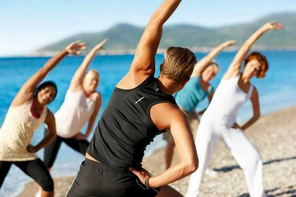 Gruppe von Frauen und Männern, die Yoga am Strand des Doryssa Seaside Resort machen