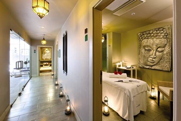 Spa-Behandlungsraum im Gran Castillo Tagoro Familien & Spaß mit weißem Behandlungstisch, roten Rosen und goldener Buddha-Wanddekoration.